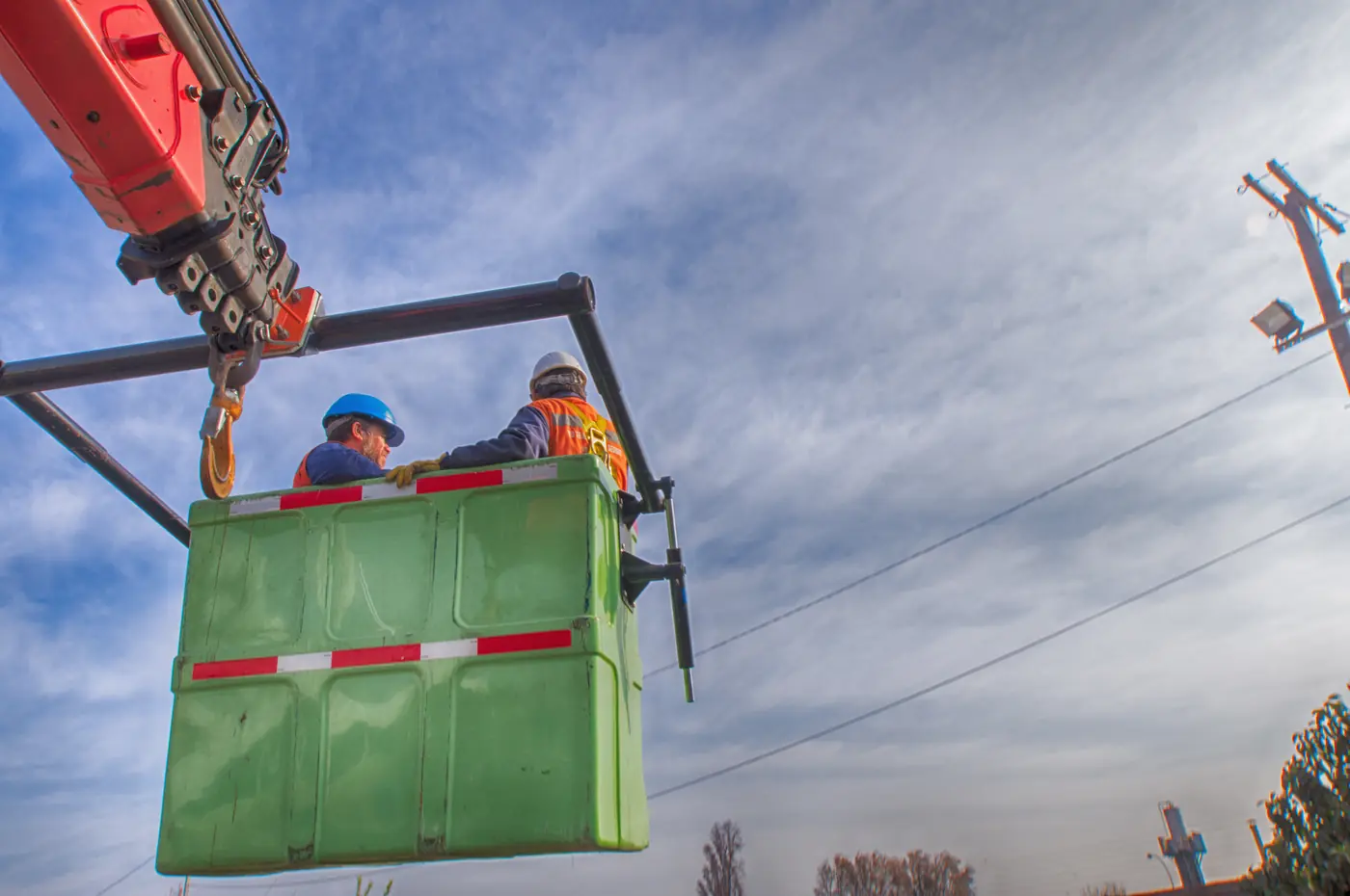 Operarios trabajando en canastillo elevado por camión grúa pluma